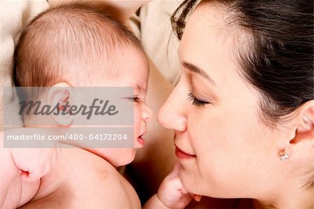 Face of baby and mother together, infant expressing anger and holding fist ready to punch.