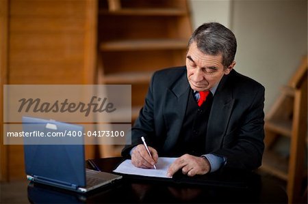 Senior businessman writing and working with document indoors