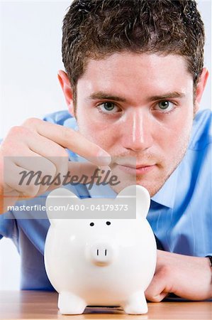 Stock image of man depositing coin into piggy bank