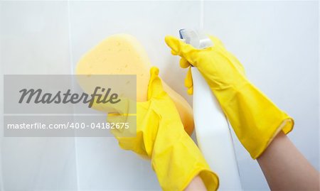 Close-up of a woman cleaning a bathroom with a sponge and detergent spray