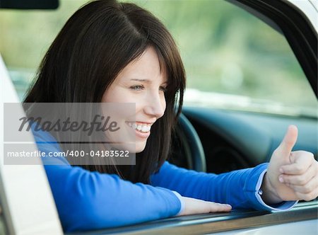 Smiling teen girl with a thumb up sitting in her car after having her driver's licence