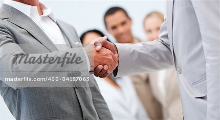 Two businessmen shaking hand in front of their colleagues in the office