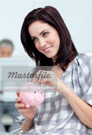 Delighted businesswoman saving money in a piggy-bank at her desk