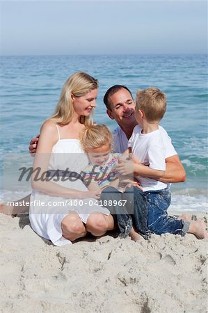 Cute children and their parents sitting on the sand at the beach