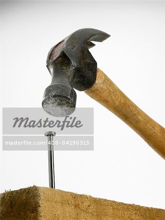 Seen from below a hammer in close proximity to the nail in wood against a white background