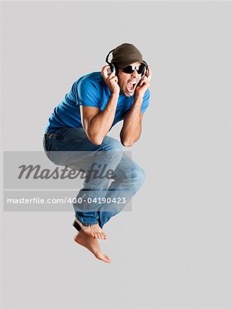 Young man jumping and listening music isolated over a gray background