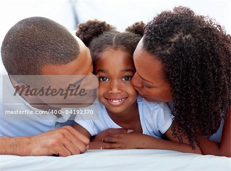 Loving parents kissing their daughter lying on a bed