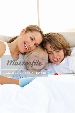 Beautiful mother and her children reading book lying in bed
