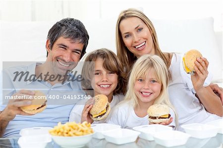 Happy family eating hamburgers sitting on the floor at home