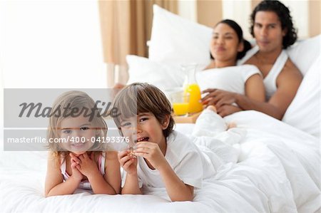Happy siblings having breakfast with their parents lying on the bed