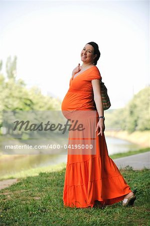 beautiful young happy pregnant woman outdoor in bright nature in orange dress