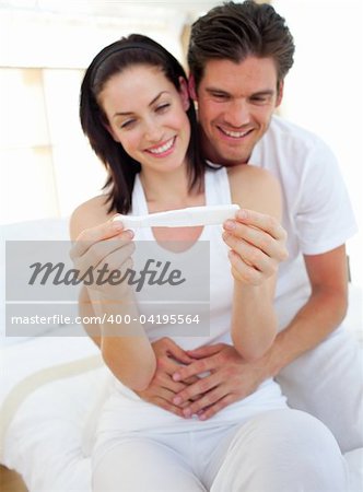 Smiling couple finding out results of a pregnancy test sitting on  bed