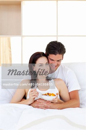 Smiling couple having breakfast lying in the bed