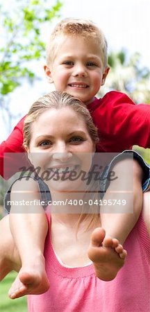 Close-up of a smiling mother giving her son a piggyback ride in a park