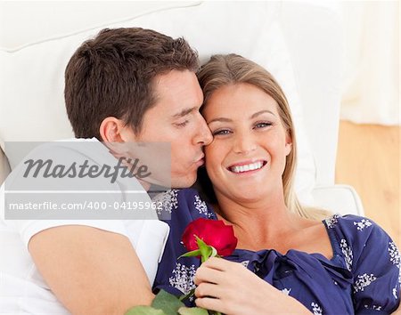 Portrait of a charming man kissing his wife lying on sofa at home