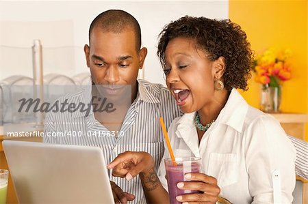 Two people at a cafe drinking frozen beverages and using a laptop. Horizontal shot.