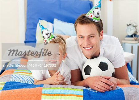 Happy child and his father playing with a soccer ball lying on bed