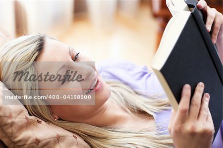 Jolly woman reading a book lying on a sofa in a living-room
