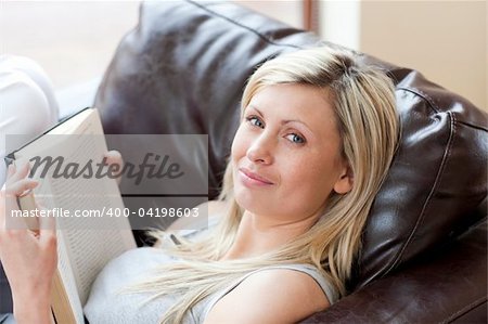 Charming woman reading a book sitting on a sofa in a living-room