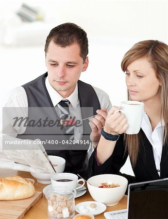 Young couple of business people reading a newspaper while having breakfast at home