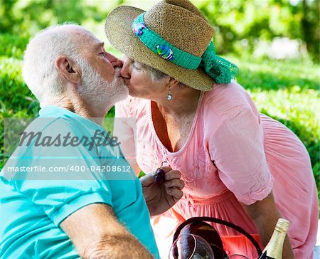 Senior couple on a picnic, kissing in the park.