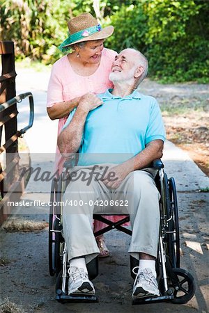 Disabled senior man in wheelchair with his loving wife taking care of him.