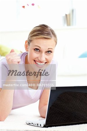 Cheerful young woman using her laptop looking at the camera in the living-room