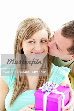 Attractive boyfriend giving a present and a kiss to his smiling girlfriend against white background