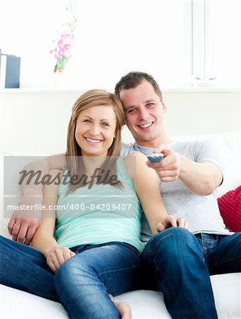 Glowing young couple sitting on the sofa watching tv in the living room