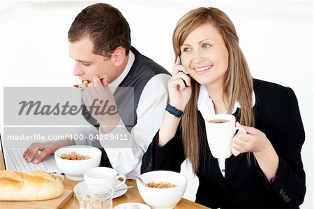 Ambitious businesswoman talking on phone while havin breakfast with her husband at home