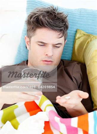 Sick caucasian man taking pills with water lying on the sofa