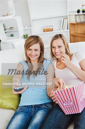 Joyful female friends watching television and eating popcorn sitting in the living-room