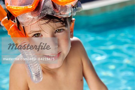 A happy young boy relaxing on the side of a swimming pool wearing orange goggles and snorkel