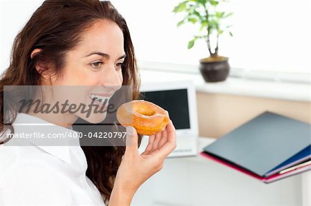 Hispanic businesswoman eating a doughnut in her office sitting at her desk
