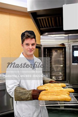 Happy baker showing his baguettes to the camera standing in his kitchen