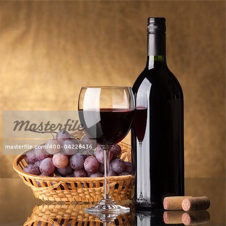 A bottle of red wine, glass and grapes on a golden background