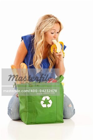 Young woman eating banana from green recycled grocery bag