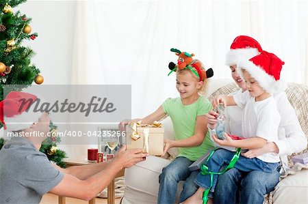 Happy father giving a present to his daughter sitting on the sofa with her mother and brother