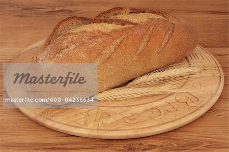 Rye bread loaf with wheat on a carved rustic wooden board against oak wood background.