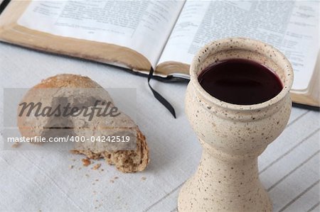 Chalice with red wine, bread and Holy Bible on a tablecloth. Shallow dof