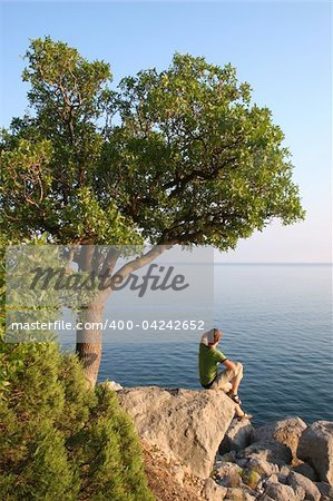 Man sitting on the rock under the tree and looking into horizon