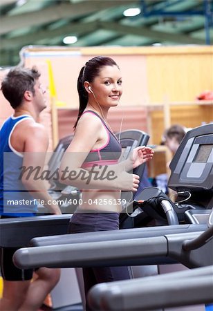 Athletic woman listening to the music while using a treadmill in a sport centre with her boyfriend