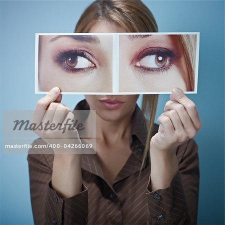 mid adult business woman holding photo of her eyes looking at different sides on blue background. Square shape, front view, waist up