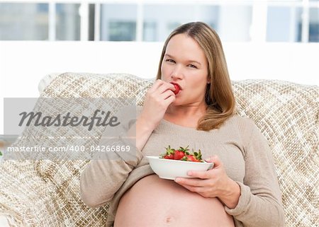 Young pregnant woman eating a strawberry sitting at home