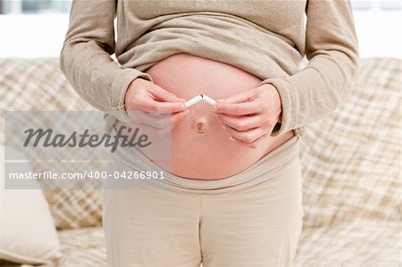 Close up of a pregnant woman breaking a cigarette standing in the living room