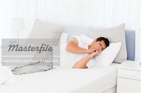 Sick man blowing his nose lying on his bed at morning