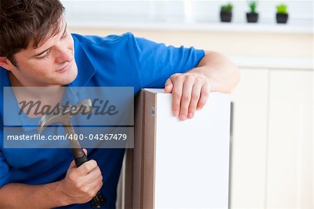 Young man building furniture using a hammer and a nail at home