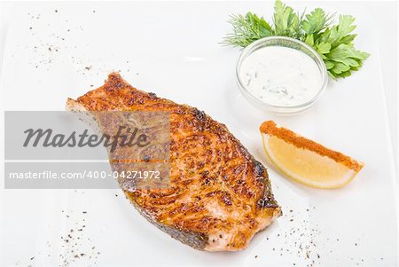 Grilled fish with sauce, lemon and greens on white plate