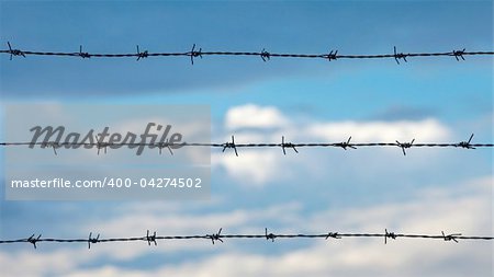 Barbed wire against cloudy blue sky