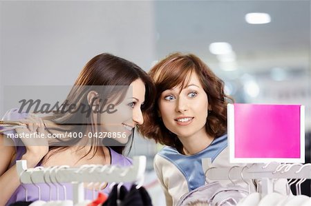 Two surprised girl-friends consult with each other in clothes shop